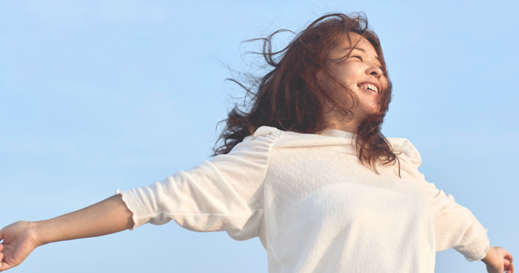 青い空の下で笑顔で清々しい様子の女性